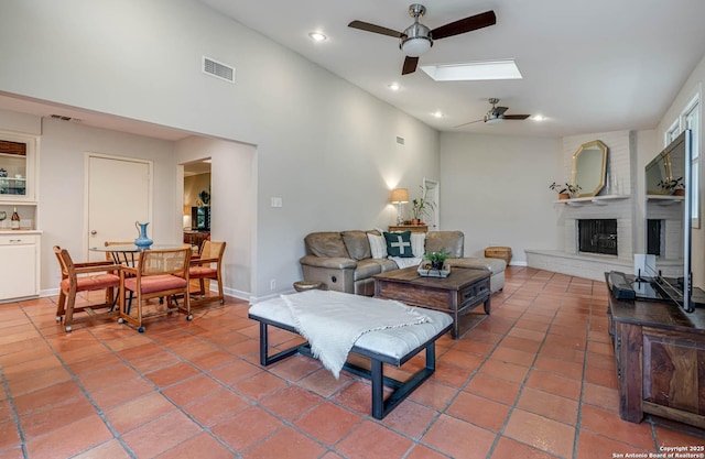 tiled living room featuring ceiling fan, a fireplace, and a skylight