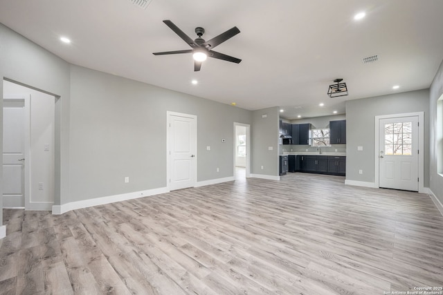 unfurnished living room with ceiling fan, sink, and light wood-type flooring