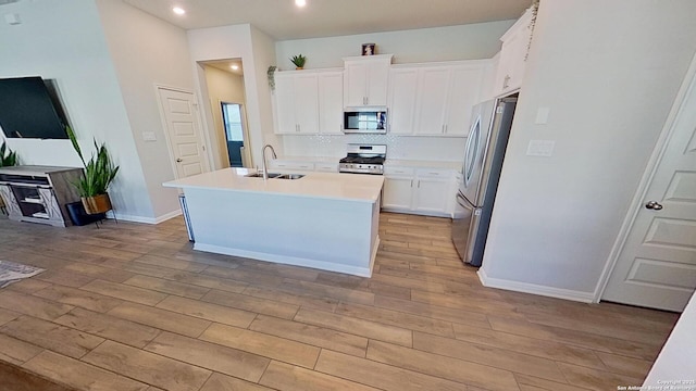 kitchen with sink, white cabinetry, light wood-type flooring, stainless steel appliances, and a kitchen island with sink