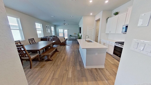 kitchen with appliances with stainless steel finishes, white cabinetry, sink, a kitchen island with sink, and light wood-type flooring