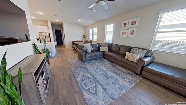 living room with ceiling fan, vaulted ceiling, and light hardwood / wood-style flooring