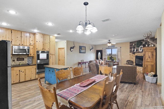 dining space with ceiling fan, a stone fireplace, and light hardwood / wood-style flooring