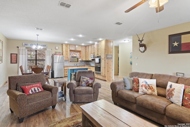 living room with ceiling fan with notable chandelier and light wood-type flooring