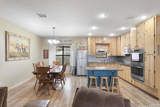 kitchen with pendant lighting, a kitchen breakfast bar, stainless steel appliances, a center island, and light brown cabinetry