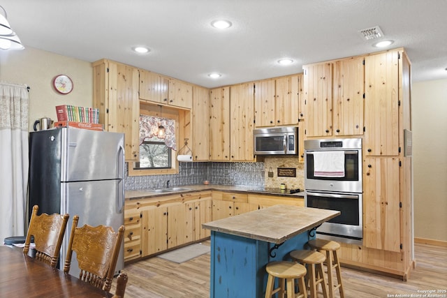 kitchen featuring a breakfast bar, sink, stainless steel appliances, light brown cabinets, and light wood-type flooring