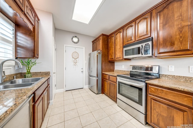 kitchen featuring a skylight, sink, light tile patterned floors, stainless steel appliances, and light stone countertops