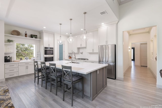 kitchen featuring appliances with stainless steel finishes, pendant lighting, sink, white cabinets, and a center island with sink