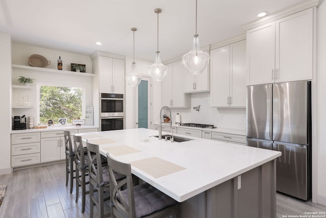 kitchen featuring white cabinetry, hanging light fixtures, stainless steel appliances, and a center island with sink