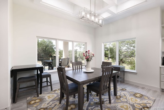 dining space with coffered ceiling, light hardwood / wood-style floors, a chandelier, and a high ceiling