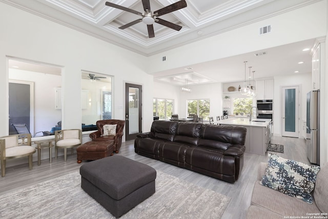 living room with coffered ceiling, crown molding, a towering ceiling, beam ceiling, and light hardwood / wood-style floors