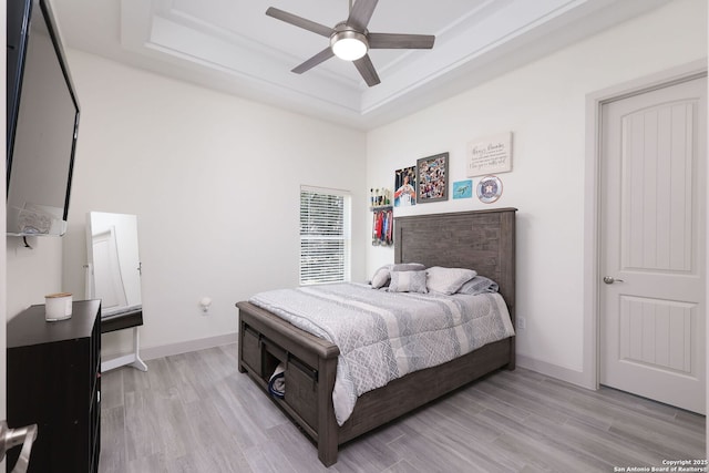 bedroom with ceiling fan, light hardwood / wood-style floors, and a tray ceiling