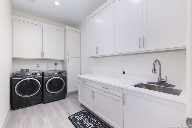 clothes washing area featuring cabinets, washing machine and dryer, sink, and light hardwood / wood-style flooring