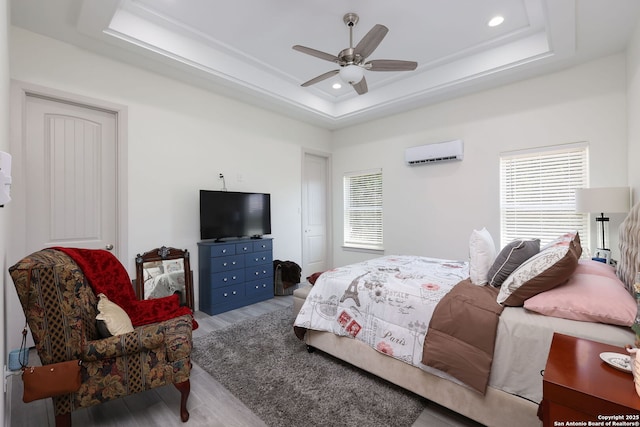 bedroom with a tray ceiling, an AC wall unit, ceiling fan, and light wood-type flooring