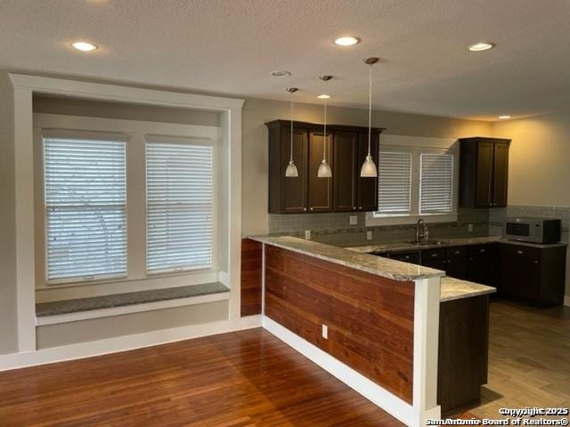 kitchen with pendant lighting, sink, light stone countertops, dark hardwood / wood-style flooring, and kitchen peninsula