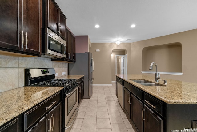 kitchen featuring sink, backsplash, stainless steel appliances, light stone counters, and an island with sink