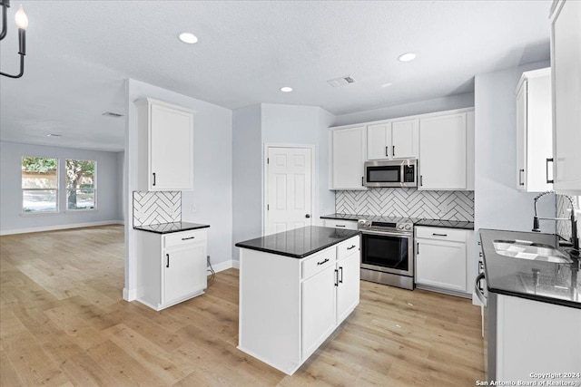 kitchen with sink, appliances with stainless steel finishes, light hardwood / wood-style floors, white cabinets, and a kitchen island