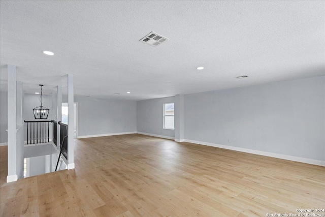 unfurnished living room with an inviting chandelier, a textured ceiling, and light wood-type flooring