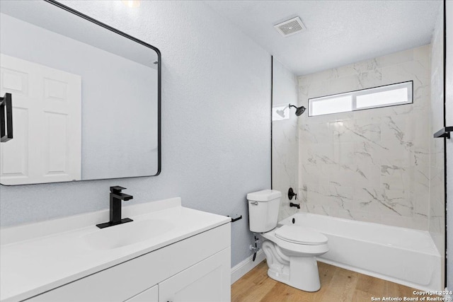 full bathroom with hardwood / wood-style floors, tiled shower / bath combo, vanity, toilet, and a textured ceiling