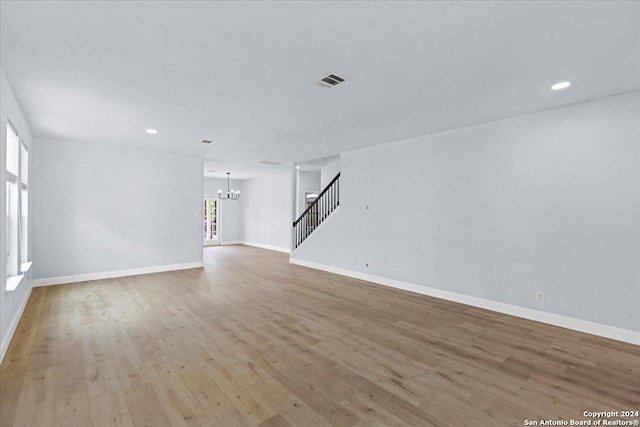 unfurnished living room featuring a chandelier and light wood-type flooring