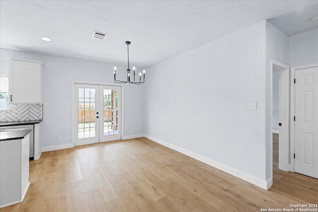 unfurnished dining area featuring french doors, an inviting chandelier, a textured ceiling, and light wood-type flooring