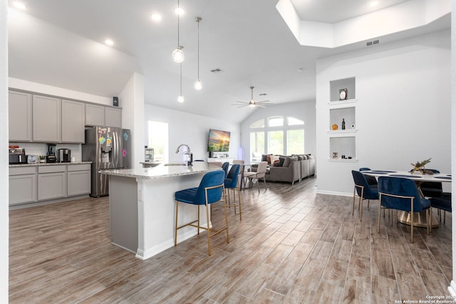 25046 Las Pilas, San Antonio, TX 78261 - kitchen with a breakfast bar, a kitchen island with sink, light stone counters, light hardwood / wood-style floors, and stainless steel refrigerator with ice dispenser