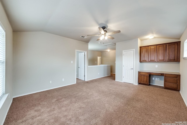 unfurnished living room featuring ceiling fan, carpet floors, built in desk, and vaulted ceiling