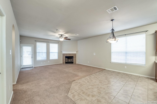 unfurnished living room featuring a tiled fireplace, light colored carpet, and ceiling fan