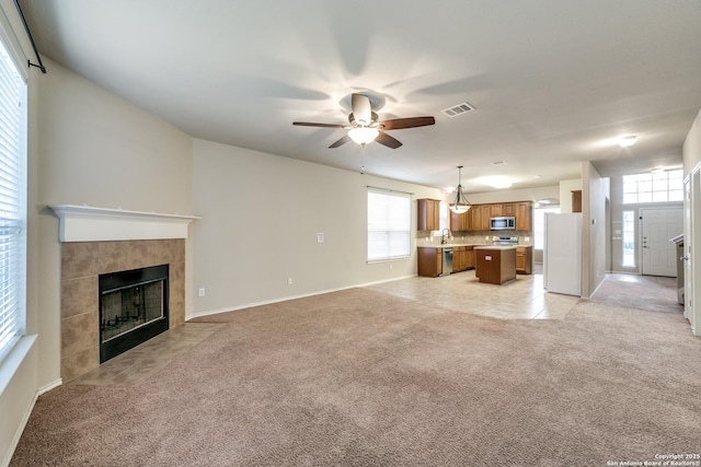 unfurnished living room featuring ceiling fan, sink, light colored carpet, and a fireplace