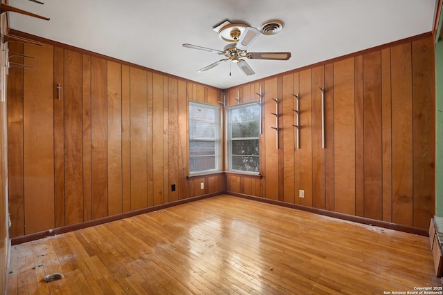 unfurnished room with ceiling fan, wooden walls, and light wood-type flooring