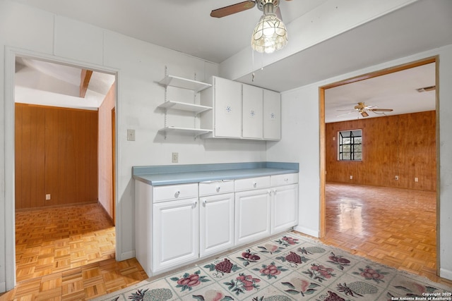 kitchen with light parquet flooring, white cabinets, ceiling fan, and wood walls