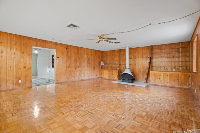 interior space featuring light parquet floors, a wood stove, ceiling fan, and wood walls