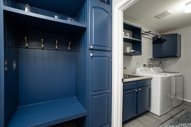 clothes washing area with sink, cabinets, independent washer and dryer, light hardwood / wood-style floors, and a textured ceiling