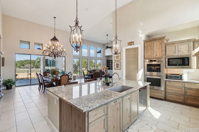 kitchen featuring built in microwave, sink, a center island with sink, pendant lighting, and stainless steel double oven