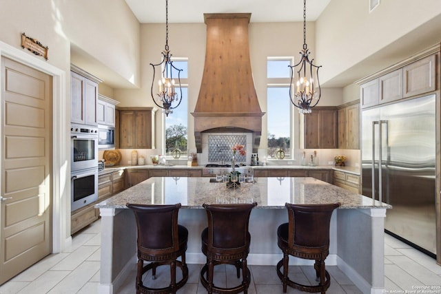 kitchen featuring a spacious island, built in appliances, light stone countertops, and custom range hood