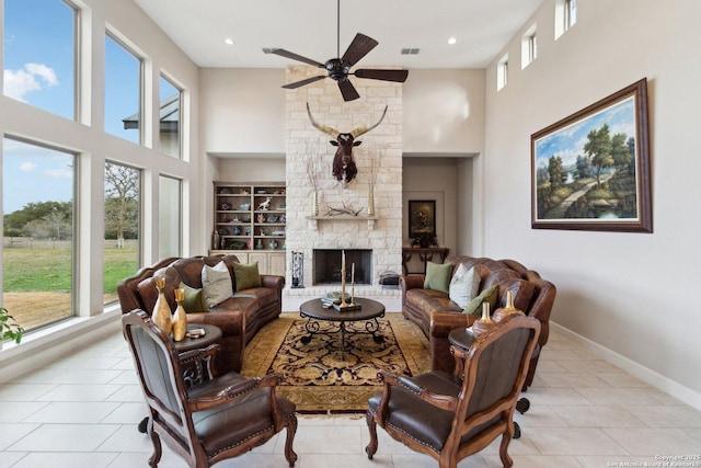 living room featuring ceiling fan, a towering ceiling, light tile patterned floors, and a fireplace