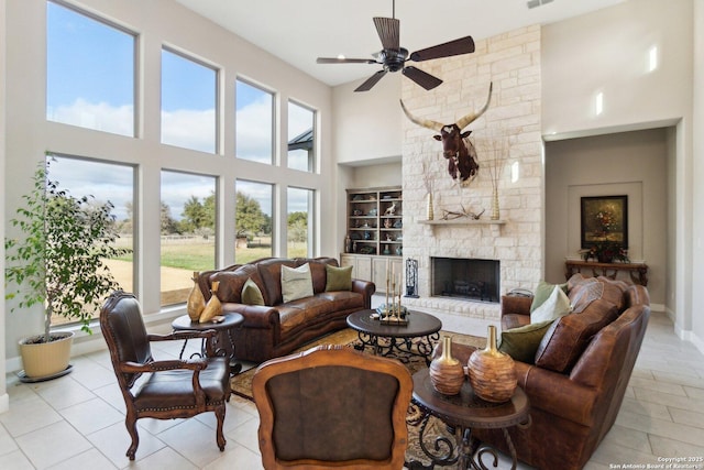 living room featuring a stone fireplace, ceiling fan, and a high ceiling