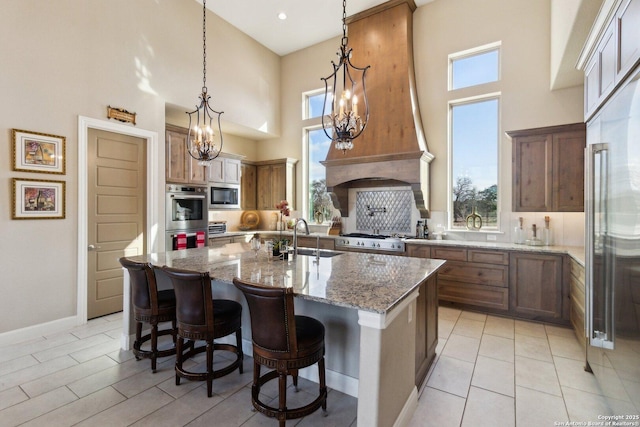 kitchen featuring pendant lighting, sink, stainless steel appliances, light stone countertops, and an island with sink