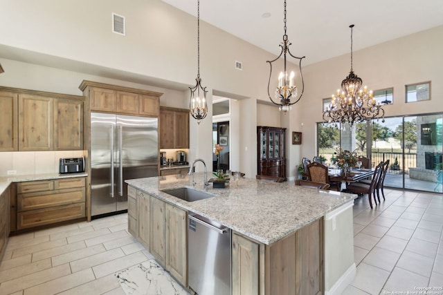 kitchen with sink, light stone counters, hanging light fixtures, stainless steel appliances, and a kitchen island with sink