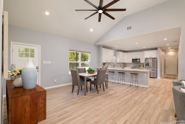 dining area featuring ceiling fan, high vaulted ceiling, and light hardwood / wood-style flooring