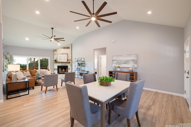 dining area featuring a stone fireplace, high vaulted ceiling, ceiling fan, and light hardwood / wood-style flooring