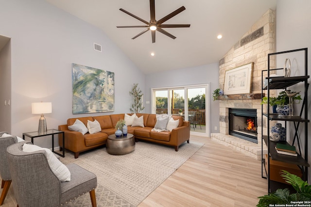 living room with ceiling fan, a stone fireplace, high vaulted ceiling, and light hardwood / wood-style flooring