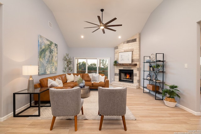 living room featuring high vaulted ceiling, a stone fireplace, light hardwood / wood-style floors, and ceiling fan