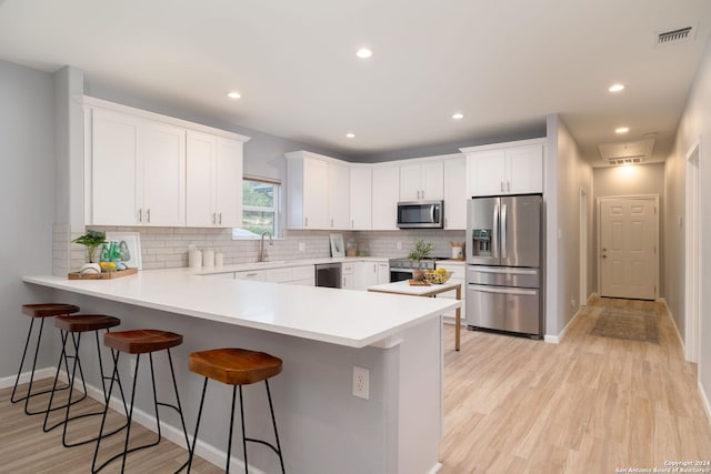 kitchen featuring kitchen peninsula, stainless steel appliances, a kitchen breakfast bar, and white cabinets