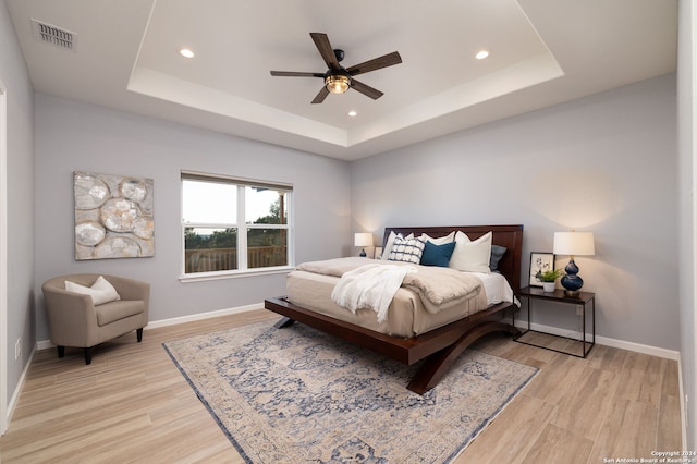 bedroom featuring ceiling fan, a raised ceiling, and light hardwood / wood-style floors