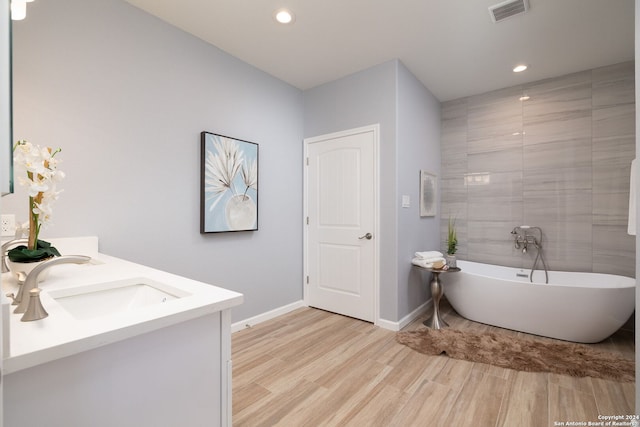 bathroom with hardwood / wood-style flooring, vanity, and a tub to relax in