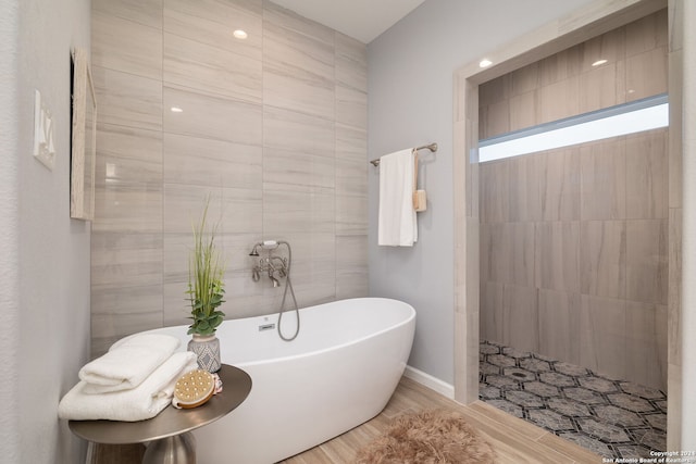 bathroom with a bath, hardwood / wood-style floors, and tile walls