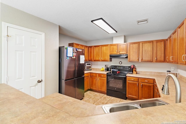 kitchen with visible vents, freestanding refrigerator, black / electric stove, under cabinet range hood, and a sink