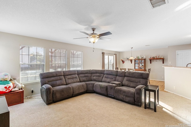 living room featuring visible vents, a ceiling fan, light carpet, a textured ceiling, and baseboards