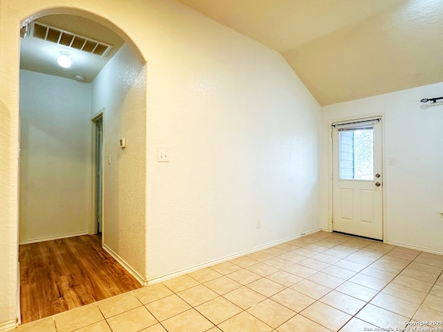 tiled empty room featuring lofted ceiling