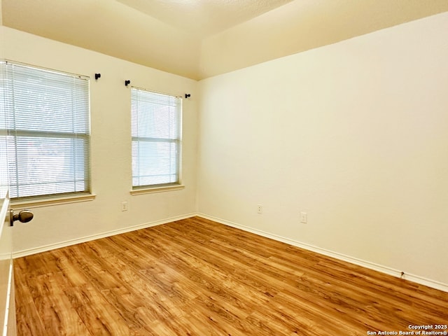 spare room with lofted ceiling and light wood-type flooring